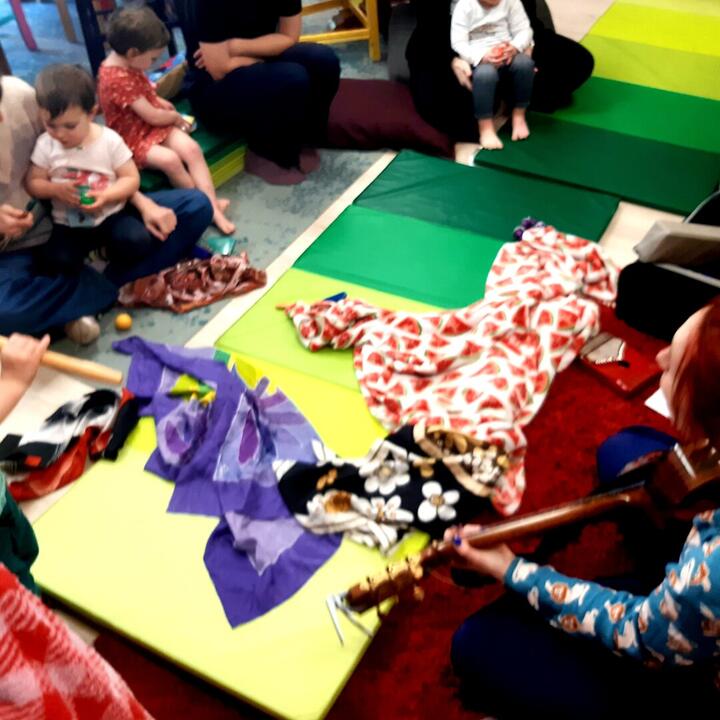 Karo met gitaar speelt muziek voor kinderen. Kinderen op schoot, kind met fluit, kind met schudeitjes, matjes