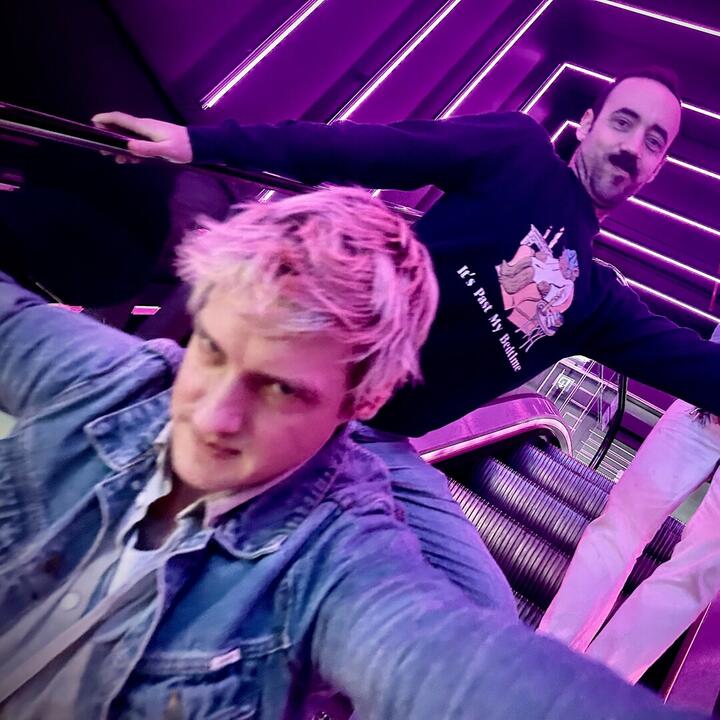 Een roltrap met mensen, paarse neonlichten, en een sweatshirt met "It's Past My Bedtime"—futuristisch en stijlvol!