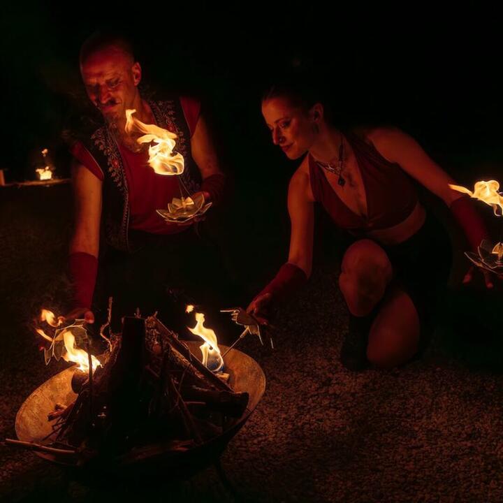 man en vrouw met vuur in de hand, terwijl ze een vuurschaal met hout aansteken