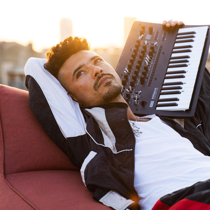 Een persoon chillt op een rode ligstoel met een Korg Minilogue synthesizer. Muziek in de maak!