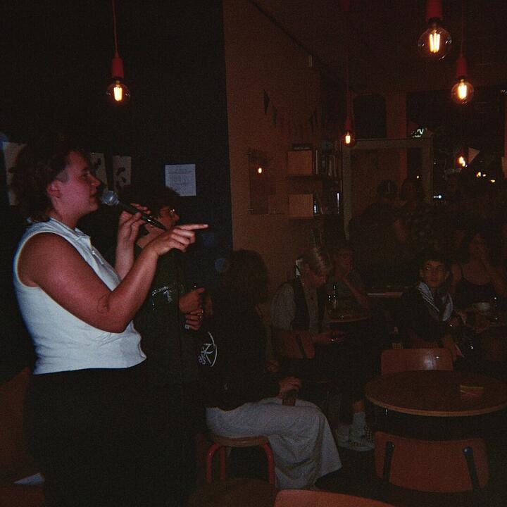 beeld van queer armworstelwedstrijd in 2025 gentse feesten in rokko, 2 mensen staan in rokko en nemen het woord voor een publiek