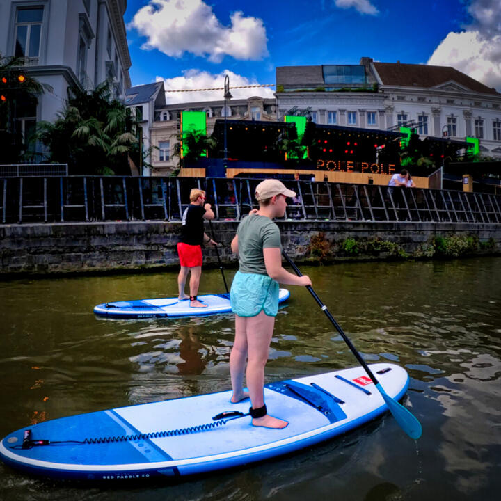 Deelnemers suppen tijdens de Gentse Feesten 2026 middag tour in het centrum van Gent langs Pole Pole aan de Korenlei  op de Leie met stadsgebouwen en festival sfeer op de achtergrond